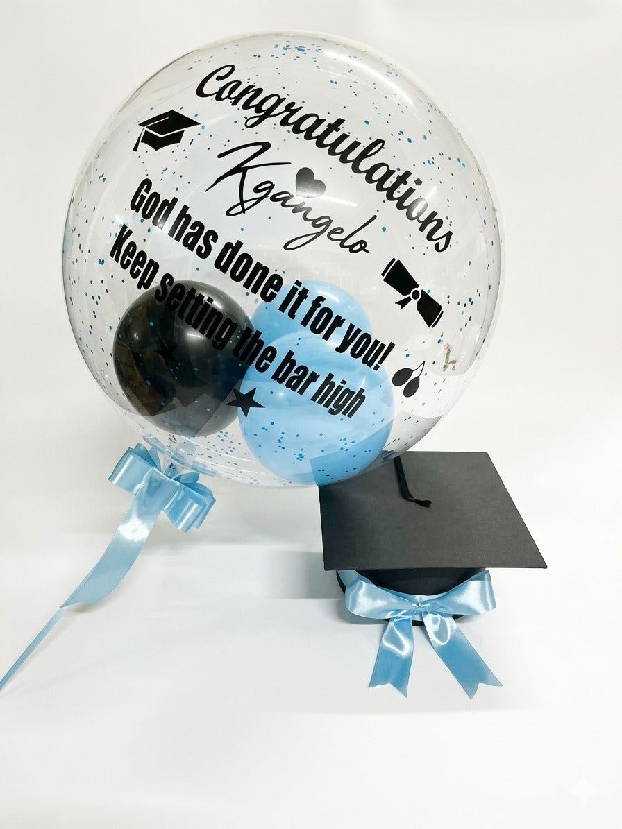 Graduation-themed decorative item with a bobo balloon, blue ribbon, and graduation cap design on a white background.