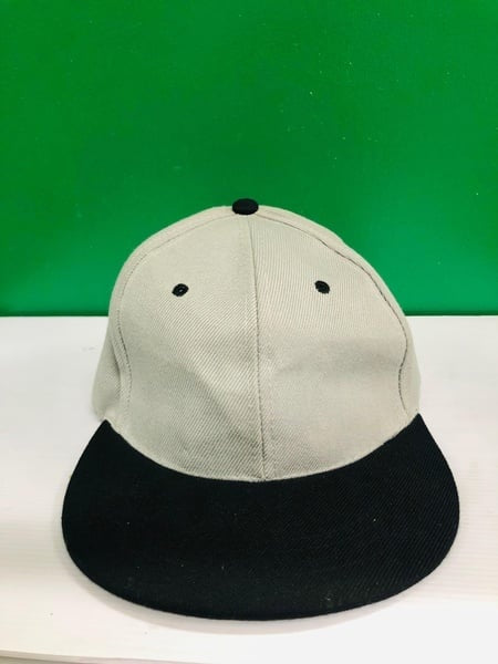Gray cap with black brim on a white surface against a green background. Gifting in Pretoria.