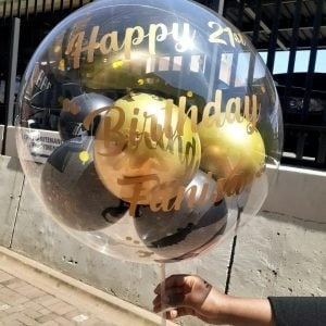 Bubble balloon with 'Happy Birthday' text held by a person outdoors.