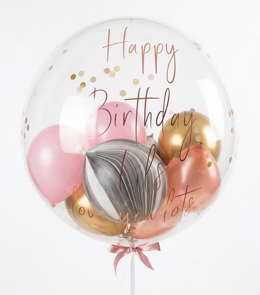 Clear balloon with pink, gold, and gray balloons inside, featuring 'Happy Birthday' text.