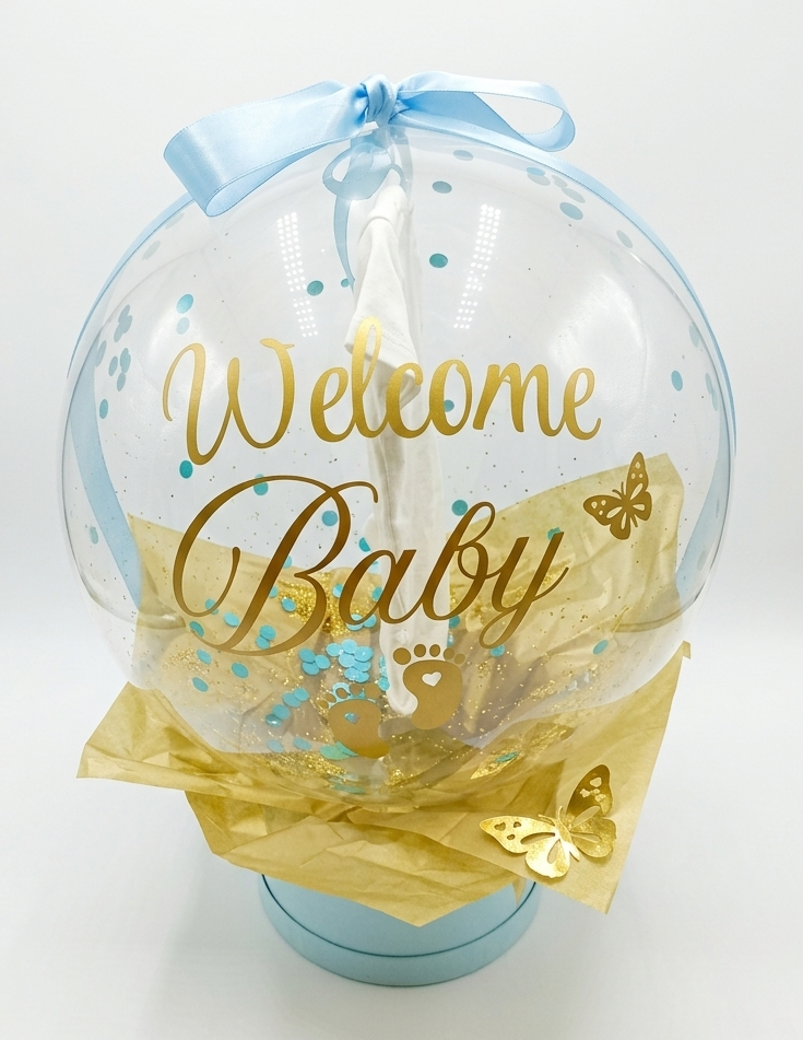 Clear balloon with 'Welcome Baby' text, blue ribbon, and gold accents on a white background