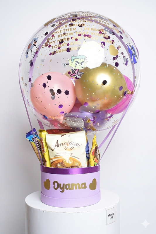 Decorative balloon with pink and gold balloons inside a transparent container, featuring a card and small items on a white background.