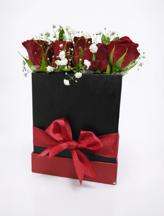 Black box with red ribbon containing red roses on a white background