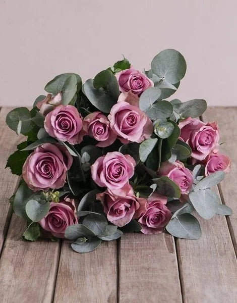 Bouquet of pink roses with green leaves on a wooden surface
