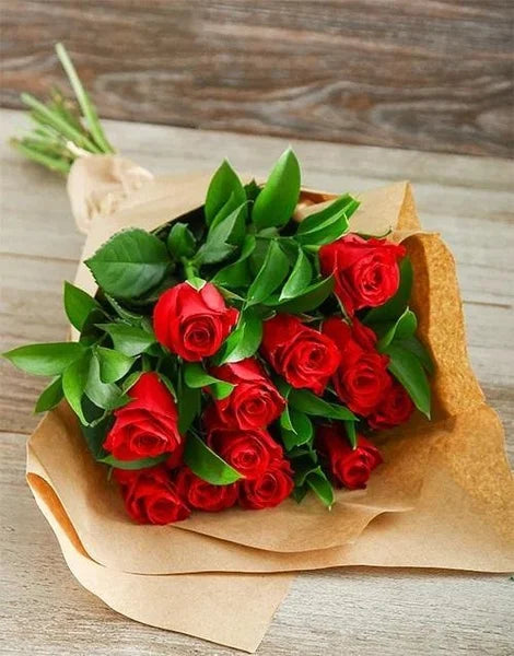 Bouquet of red roses with green leaves on brown paper against a wooden background