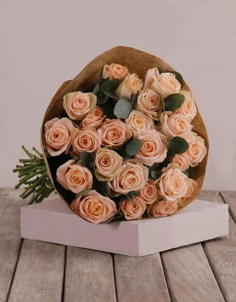Bouquet of peach roses in a brown paper wrap on a wooden surface with a light gray background