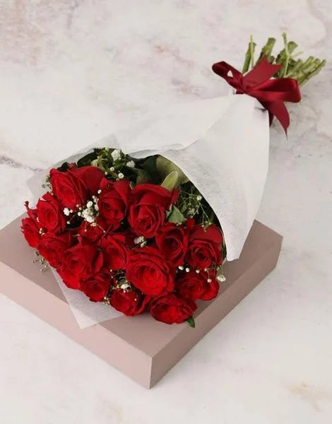 Bouquet of red roses with a white wrap on a light marble background
