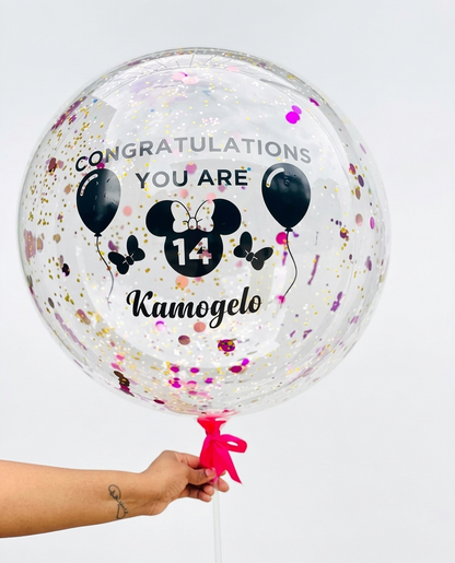 Clear balloon with personalized text and confetti, held by a person against a light gray background