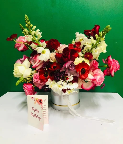 Bouquet of flowers with a 'Happy Birthday' card on a white surface against a green background