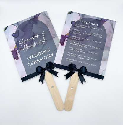 Two wedding ceremony programs on popsicle sticks with decorative ribbons against a white background.